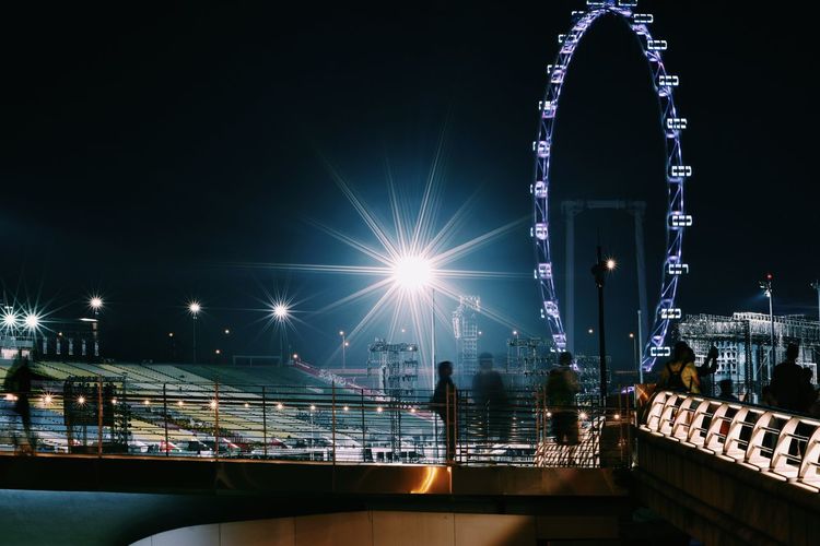 People on bridge in city against sky at night