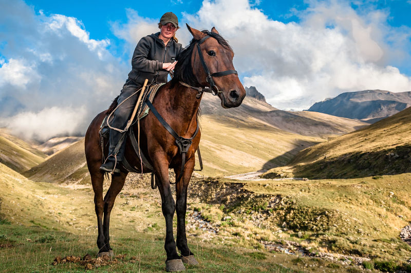 Side view of woman riding horse on mountain against sky