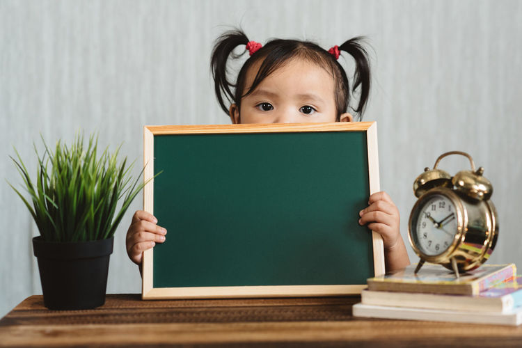 Portrait of girl holding slate on table at home