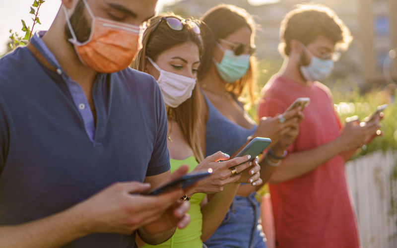 Group of friends wearing safety mask for coronavirus pandemic using smartphones