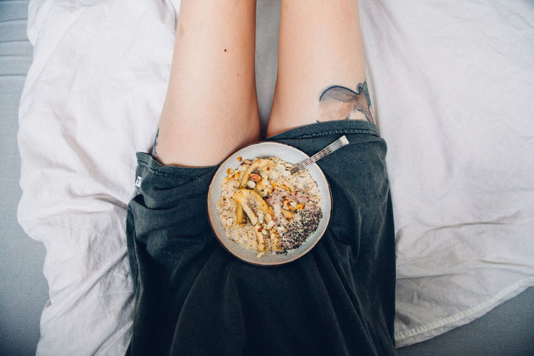 Midsection of woman with of food on bed at home