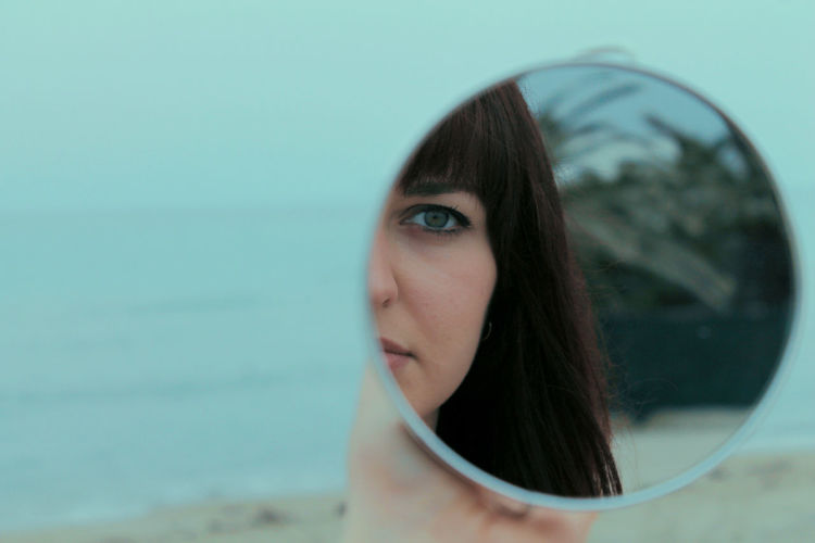 Reflection of woman in hand mirror against sea