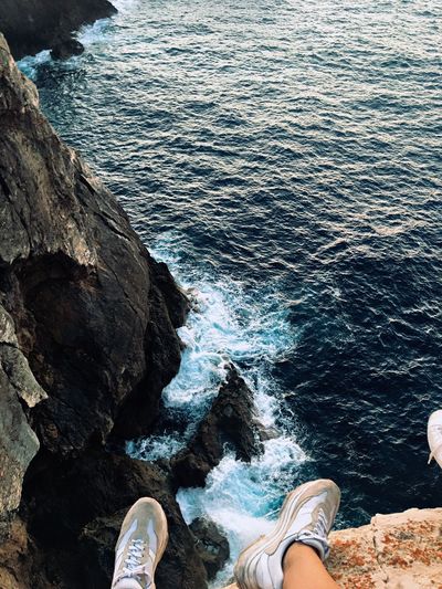 Low section of person sitting on cliff against sea