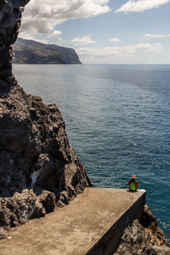 High angle view of man sitting on cliff against sea