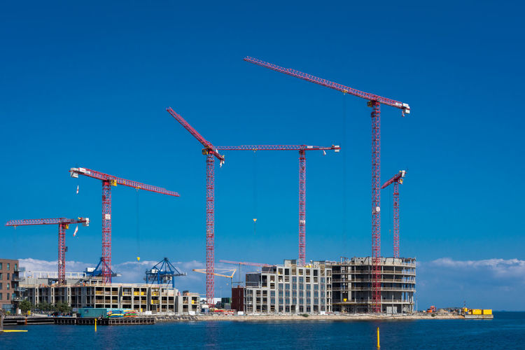 Cranes at construction site against clear blue sky