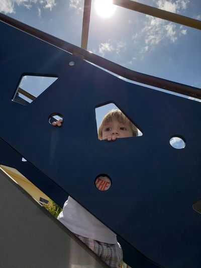 Low angle view of boy looking through outdoor play equipment in playground