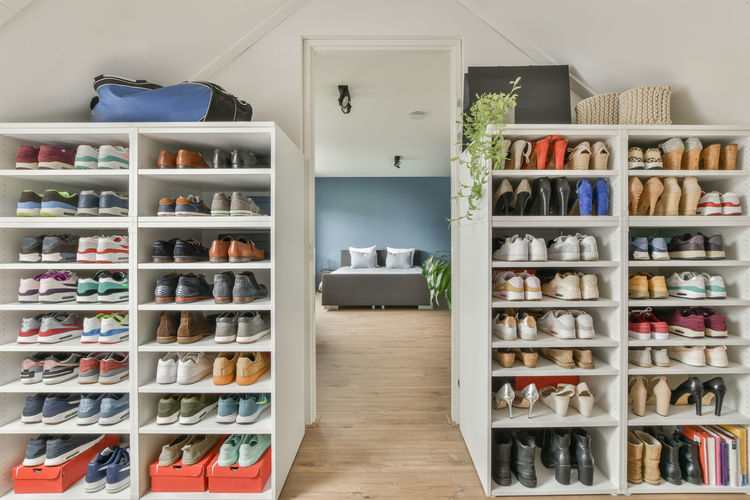 Modern shelves with various footwear located near opened door to bedroom in attic