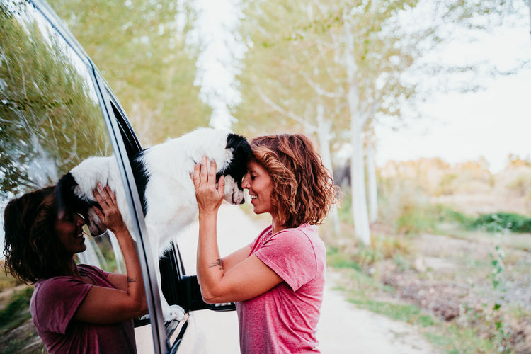 Side view of woman holding dog through car window