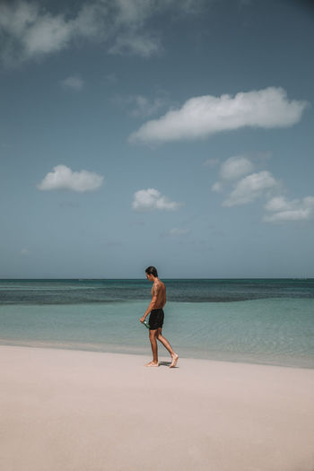 Shirtless man walking at beach against sky