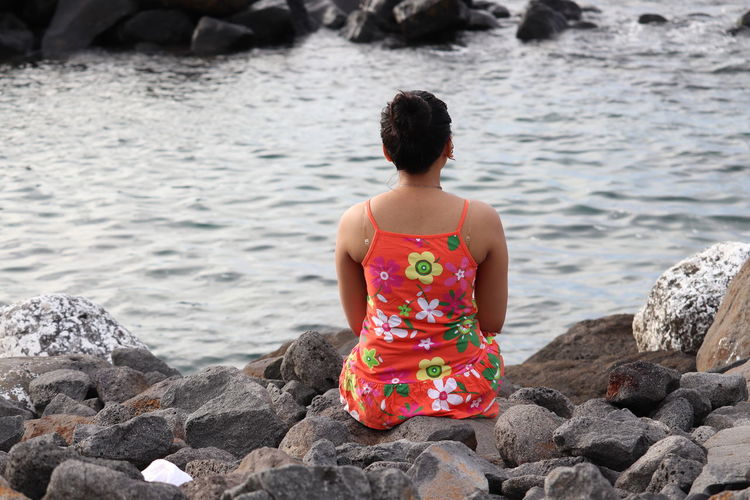 Rear view of woman sitting on rock by sea