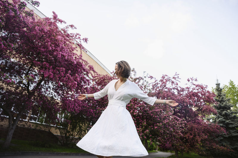 Woman wearing white dress with arms outstretched in apple blossom garden