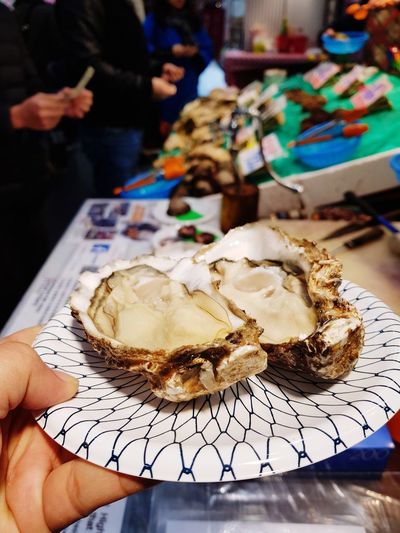 Cropped image of hand holding seashells in plate at market stall