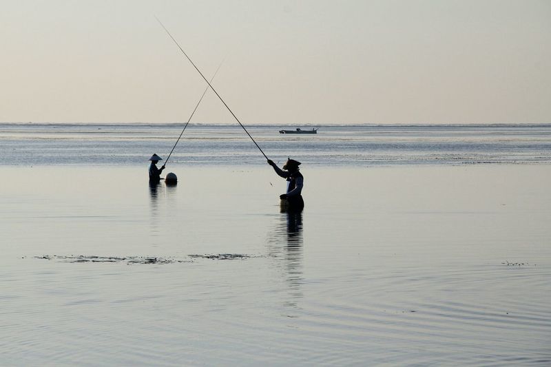 Men fishing in sea against clear sky
