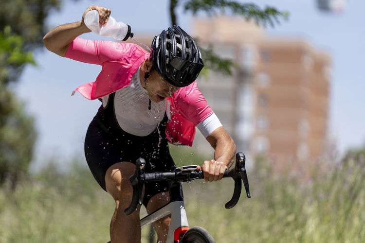 Cyclist riding bicycle pouring water from bottle on sunny day