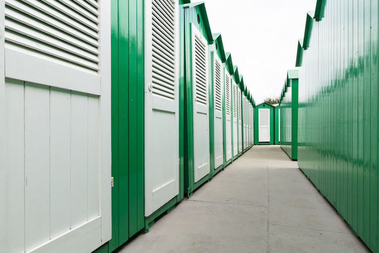 View down a row of green painted wooden beach cabins with white doors