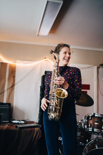 Happy young female musician playing saxophone in rehearsal studio