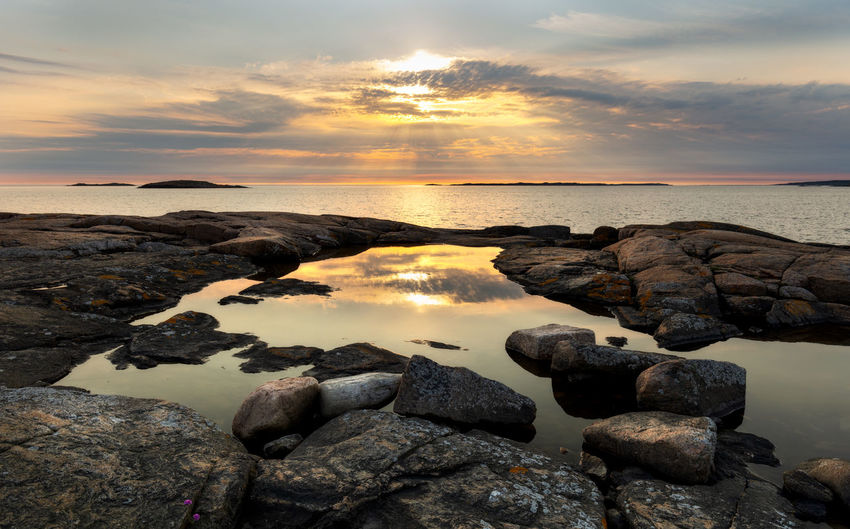 Rocks on sea shore against sky during sunset