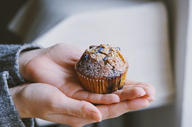 Cropped hands holding cupcake at home