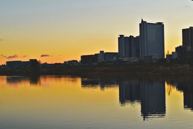 Buildings by lake against sky during sunset