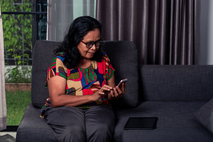 Old woman using mobile phone while sitting on sofa