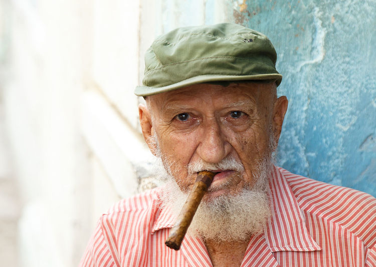 Portrait of senior man wearing cap smoking cigar while sitting outdoors