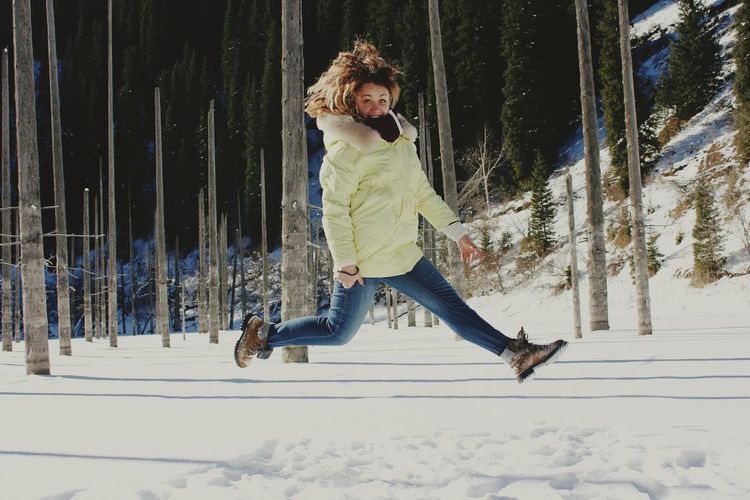 Full length of young woman jumping in snow
