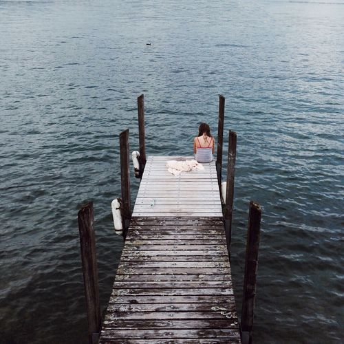 High angle view of woman sitting on pier over calm lake