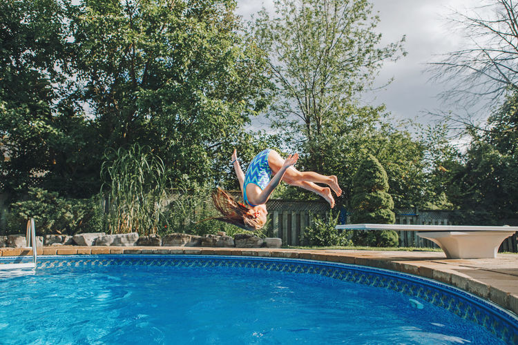 Girl jumping in swimming pool against trees