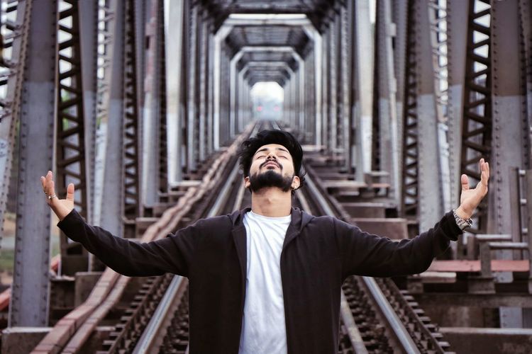 Young man with arms outstretched standing on railway bridge
