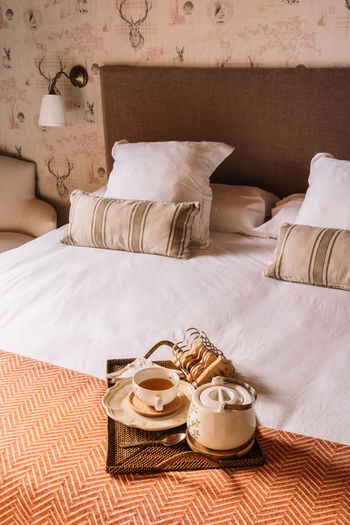From above of tray with waffles with tea in cup and kettle placed on soft bed in morning