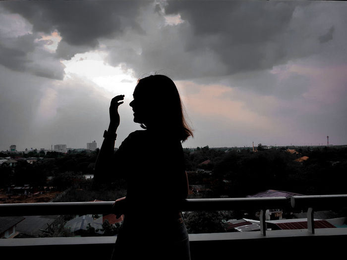 Side view of silhouette woman photographing cityscape against sky