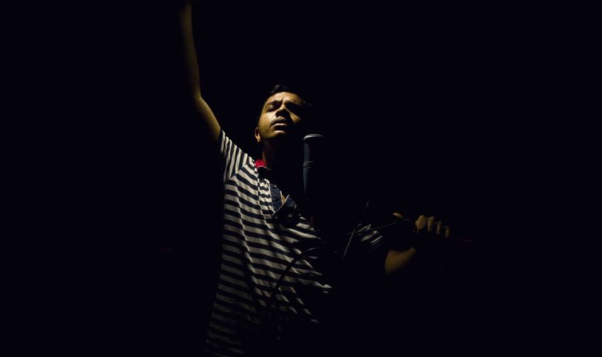 Young man singing in dark at recording studio