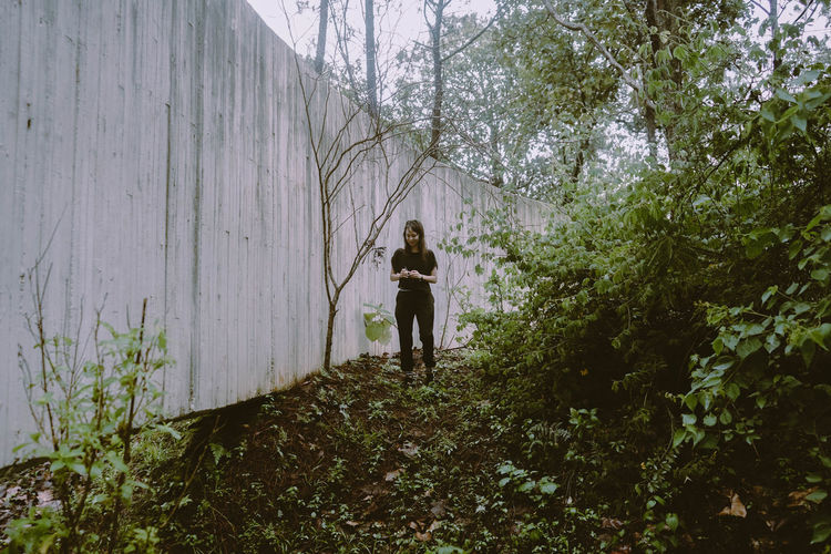 Full length of woman standing by retaining wall in forest