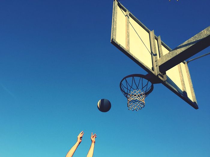 Cropped hands playing basketball against clear sky