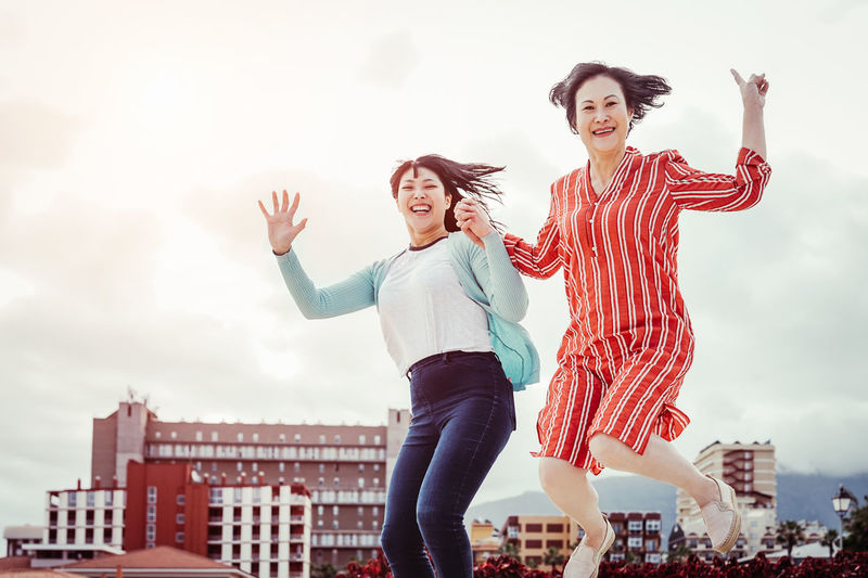 Portrait of smiling women jumping against sky in city