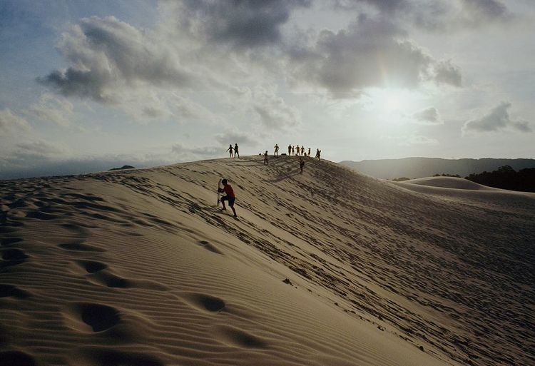 People walking on desert against sky during sunset