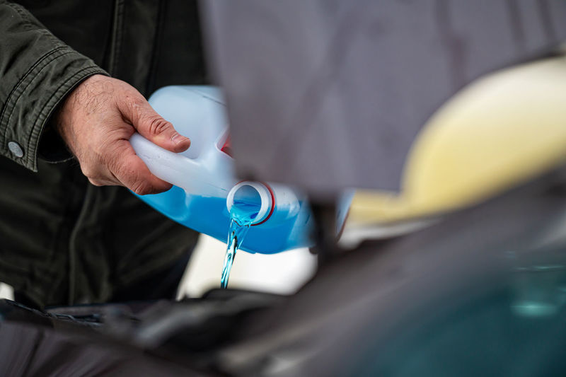 Driver refilling the blue non-freezing windshield washer liquid in the tank of the car, closeup