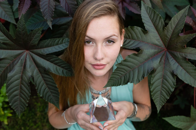 Portrait of young woman holding prism while standing against plant