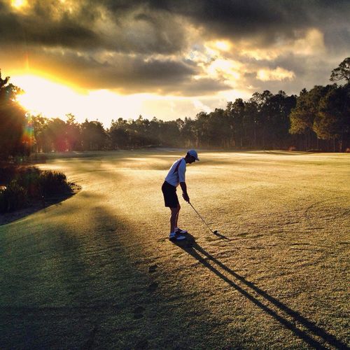 Full length of man on golf course against sky during sunset