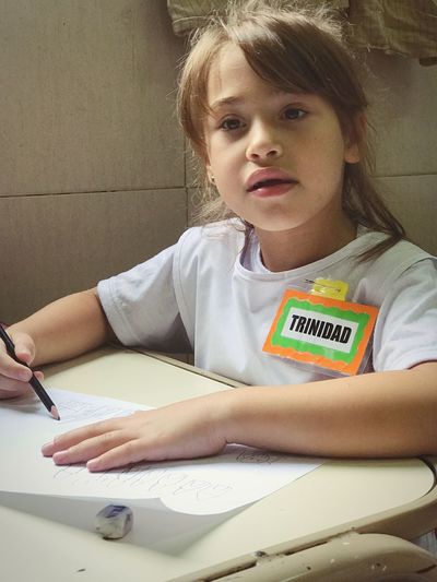 Girl with name tag writing on paper at desk in school