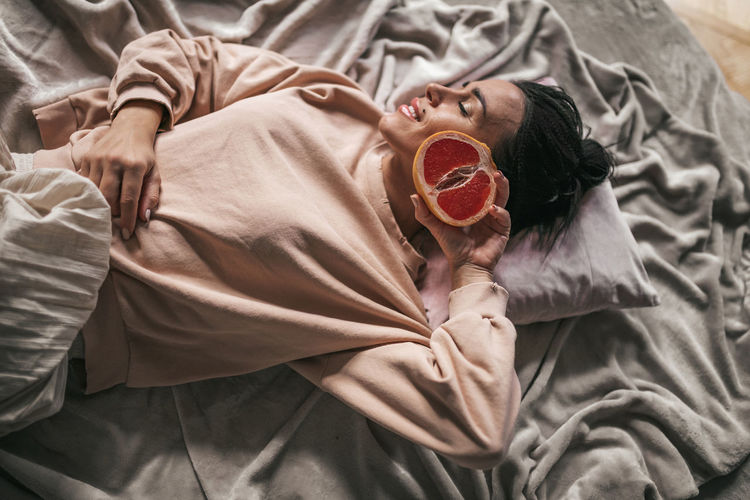 High angle view of woman holding fruit lying on bed