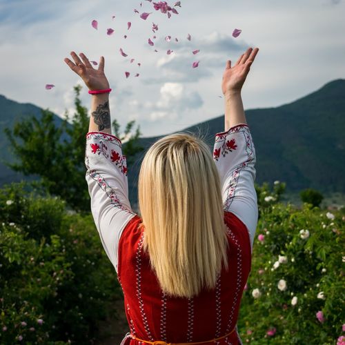 Rear view of woman throwing petals against sky
