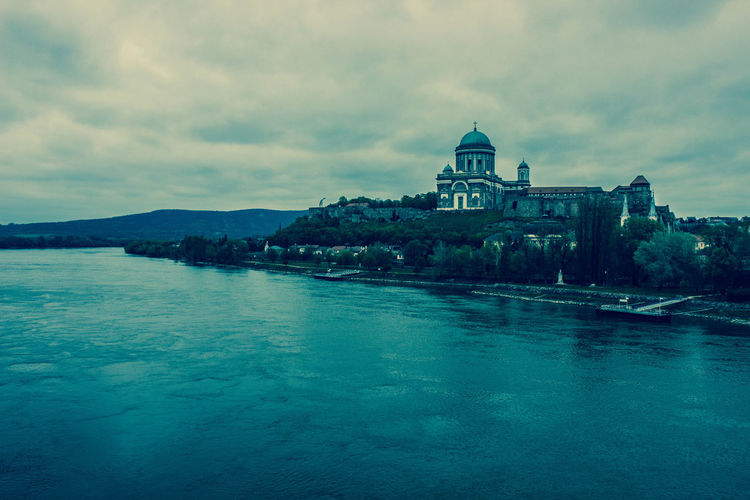 View of church by river against cloudy sky