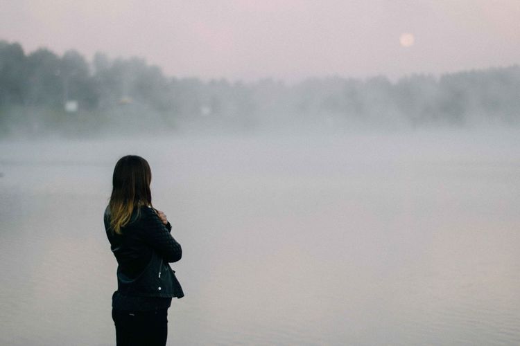 Woman standing by lake during foggy weather