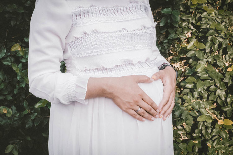 Midsection of pregnant woman standing by plants