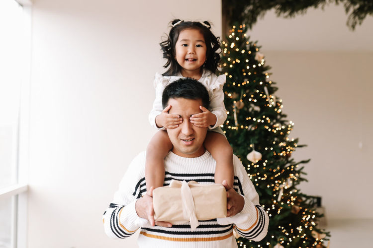 Funny dad and little daughter in sweaters are holding a gift box for the christmas holiday at home