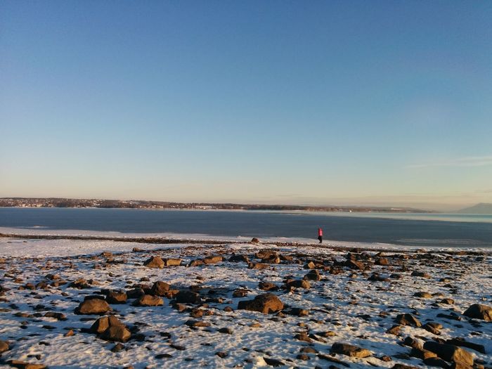 Mid distance view of person standing at frozen riverbank against sky