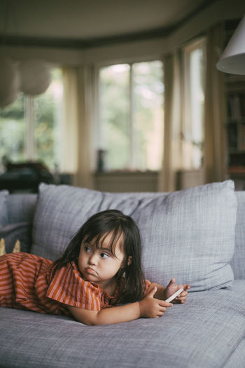 Down syndrome girl looking away while using smart phone on sofa at home
