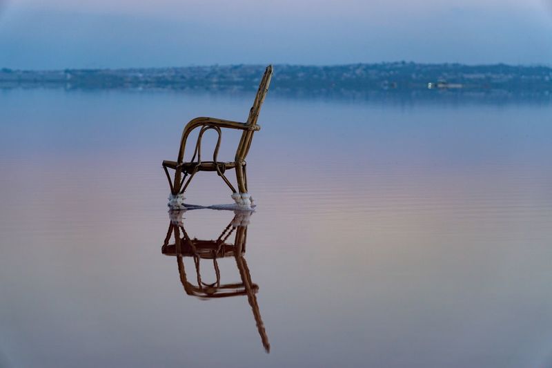 View of chair on lake against blue sky