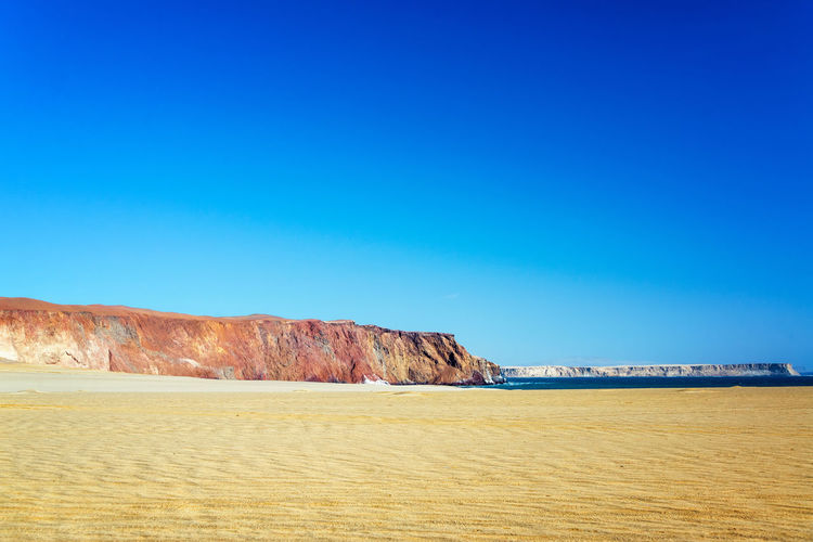 Scenic view of beach by cliff against clear sky at paracas peninsula